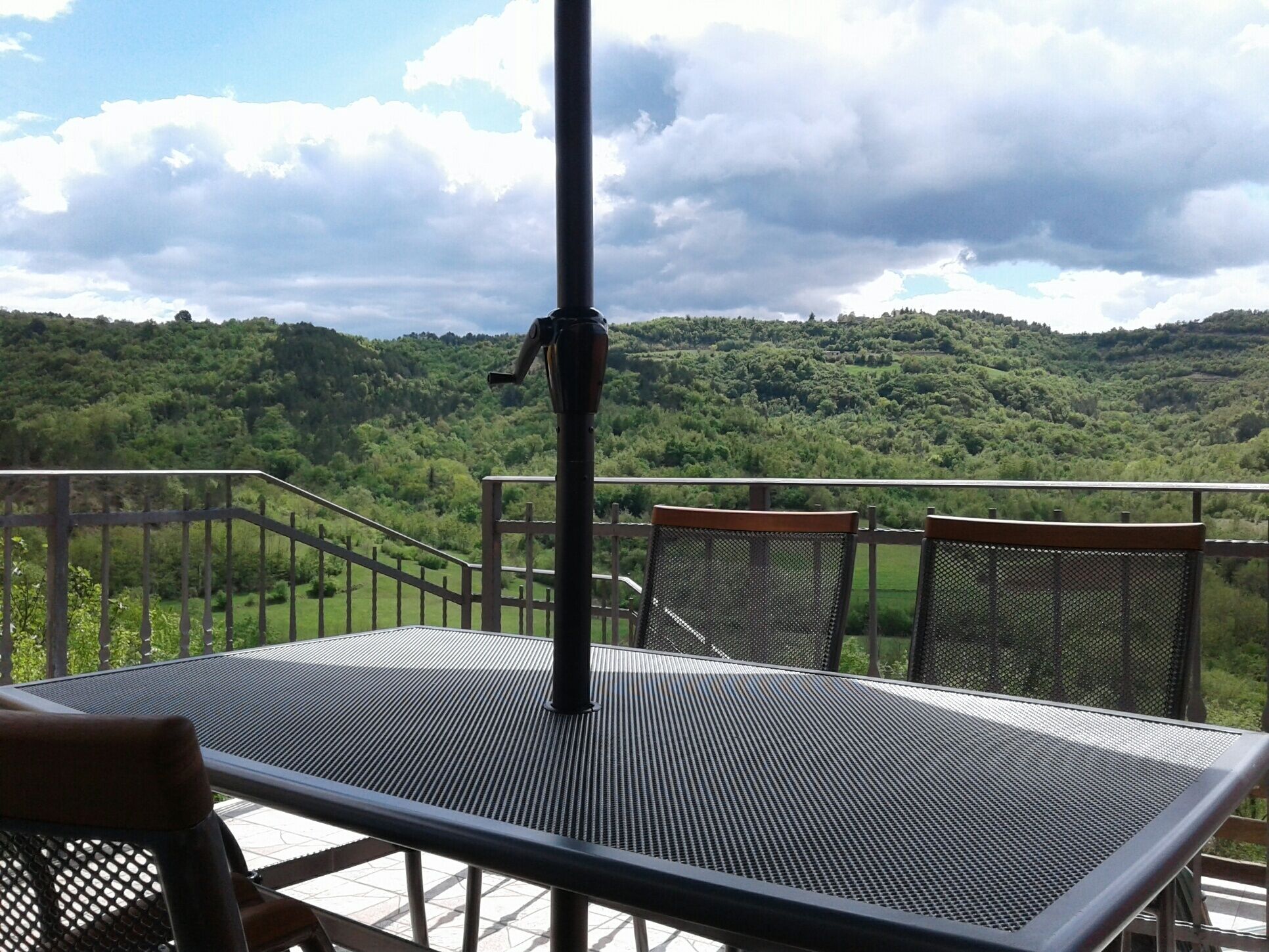 A terrace with a table and chairs, overlooking a lush green landscape with hills.
