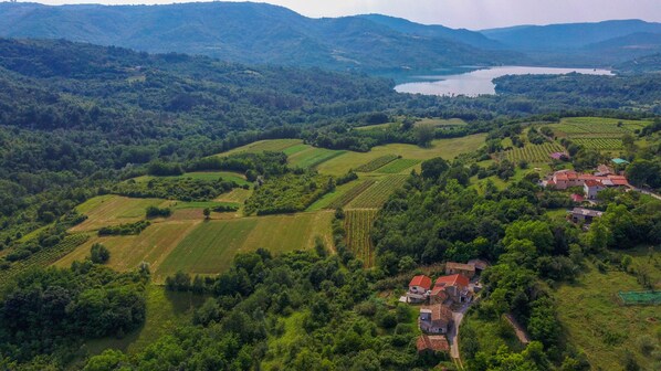 An aerial view of a rural landscape with terraced fields, a lake, and a cluster of traditional houses with red roofs.