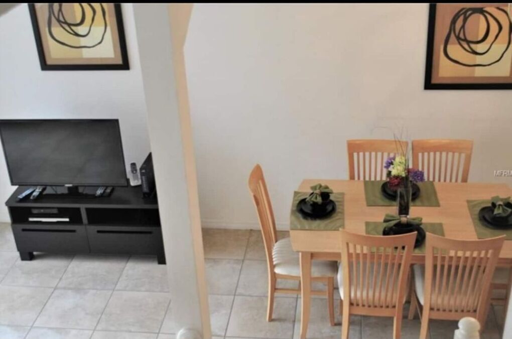 A dining area with a wooden table and chairs, a TV on a black stand, and abstract art on the walls.