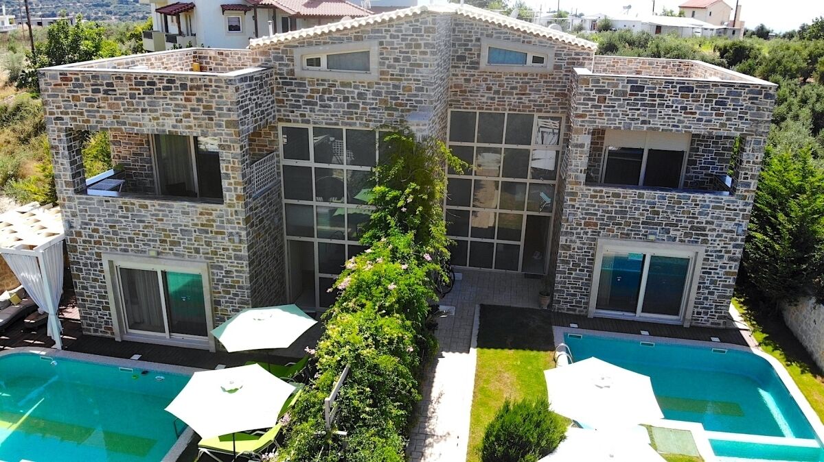 Una casa de piedra de dos pisos con piscina, mobiliario de exterior y jardín.