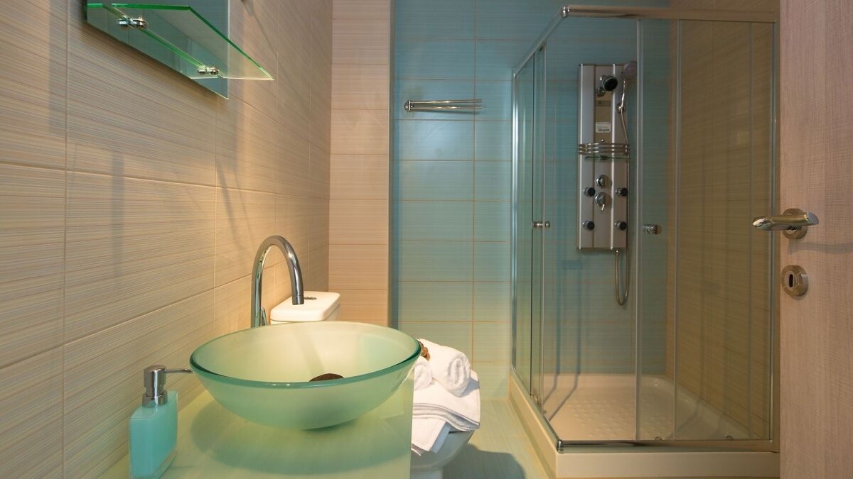 Een moderne badkamer met een glazen wasbak, een douchecabine van glas en een handdoekrek.