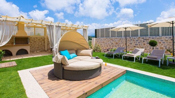 A poolside area with a round wicker sofa, lounge chairs, and a pergola with curtains. - Blue Mare Villa, privacy and relaxation! (Rethymnon)