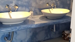 Un baño con dos lavamanos, cada uno con un espejo encima. Hay toalleros y un dispensador de jabón en la encimera.