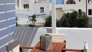 Mesa y sillas de madera bajo una pérgola blanca, con vistas a edificios blancos y un cielo azul despejado.