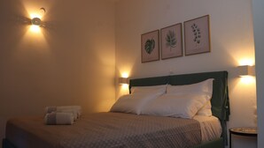 Una cama bien tendida con sábanas blancas y un cabecero verde, flanqueada por lámparas de lectura fijadas a la pared.