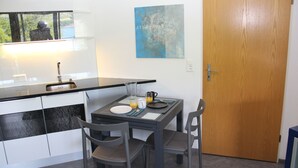 Pieni, käytännöllinen keittiö, jossa on pesuallas, ruokapöytä tuoleineen ja ovi.