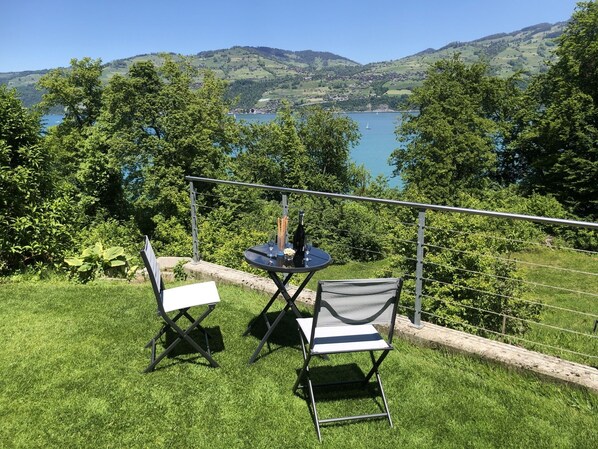 Un espace extérieur aménagé avec deux chaises et une table, offrant une vue sur un lac et des collines.