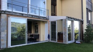 Moderni talo, jossa on lasiseinillä varustettu patio, ruokailutila pöytineen ja tuoleineen sekä pieni puutarha.