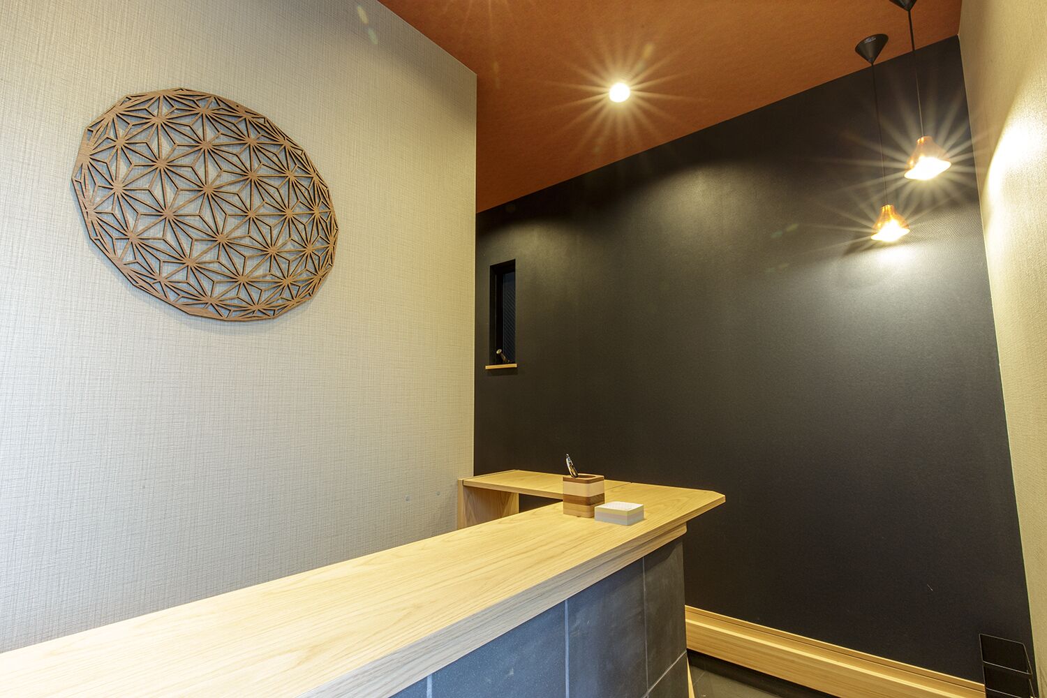 A modern bathroom with a wooden vanity, a geometric wall decoration, and pendant lighting.