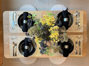 A rectangular dining table with four black plates, silverware, and a centerpiece of yellow flowers. - ORIGAMI STAY -Futatsubashicho- (Nagoya)