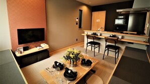 Ein modernes Hotelzimmer mit Essbereich, Flachbildfernseher, Küchenzeile und großem Fenster.