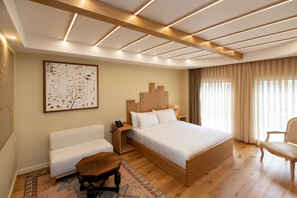 Une chambre moderne avec un lit en bois, un canapé blanc, une table de chevet en bois et un grand tableau abstrait accroché au mur.