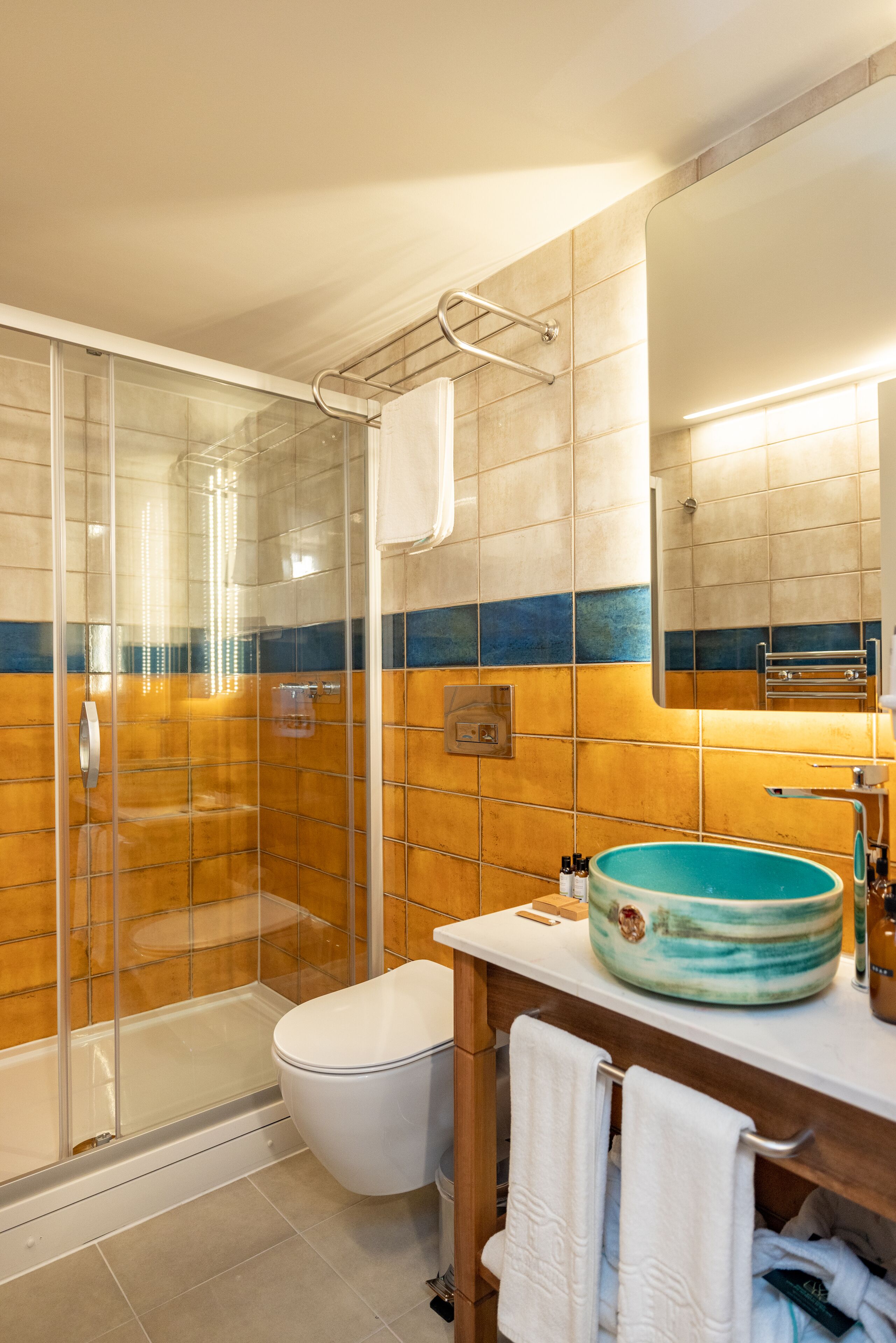 Een badkamer met een douchecabine van glas, een wit toilet, een wastafel met een blauwe kom en een spiegel boven de wastafel.