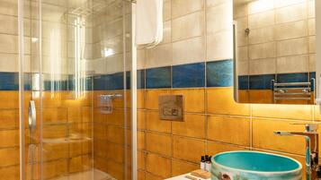 Une salle de bain avec une douche à parois de verre, des toilettes blanches, un lavabo avec un bac bleu et un miroir au-dessus du lavabo.
