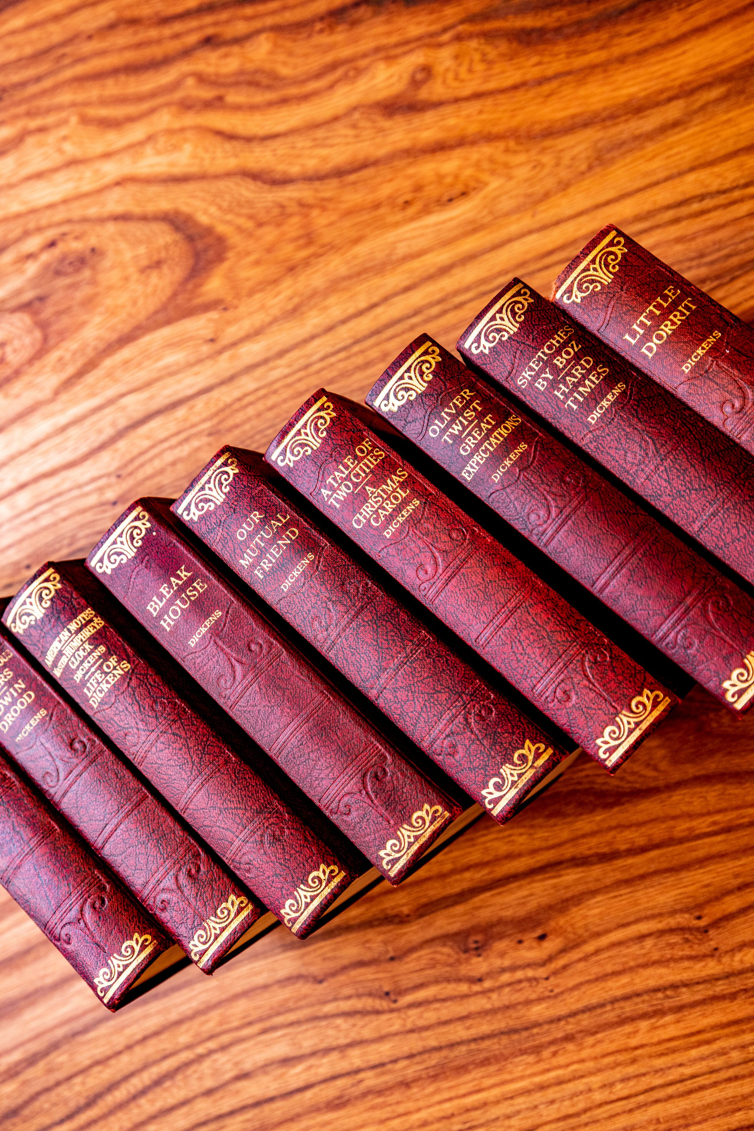 A collection of books with ornate gold detailing on their spines, arranged on a wooden surface.