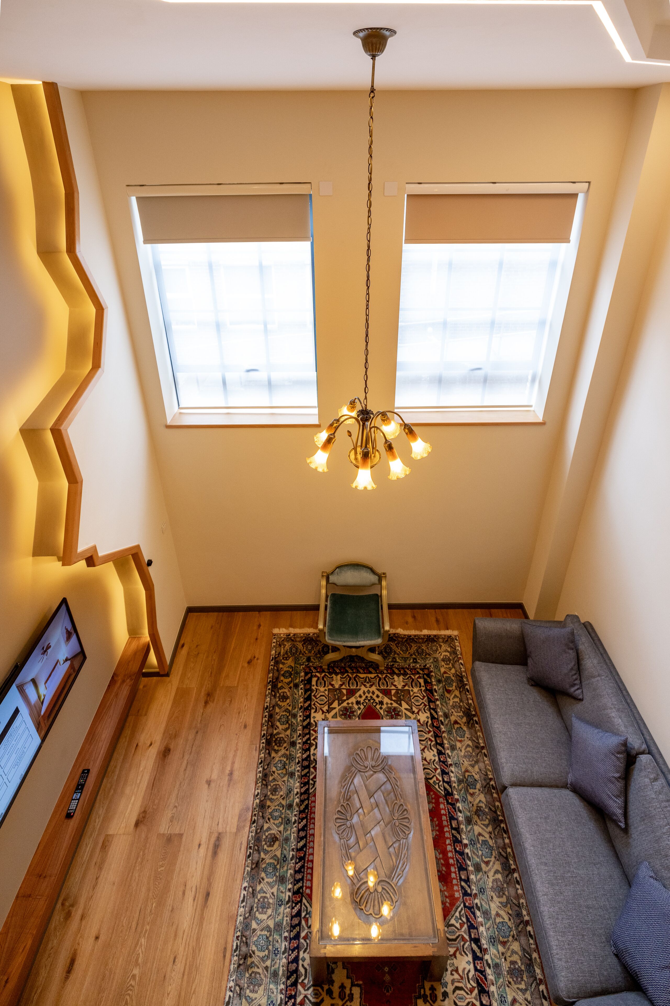 A loft-style room with a sloped ceiling, wooden flooring, a gray sofa, a patterned rug, a wooden coffee table, and a chandelier.