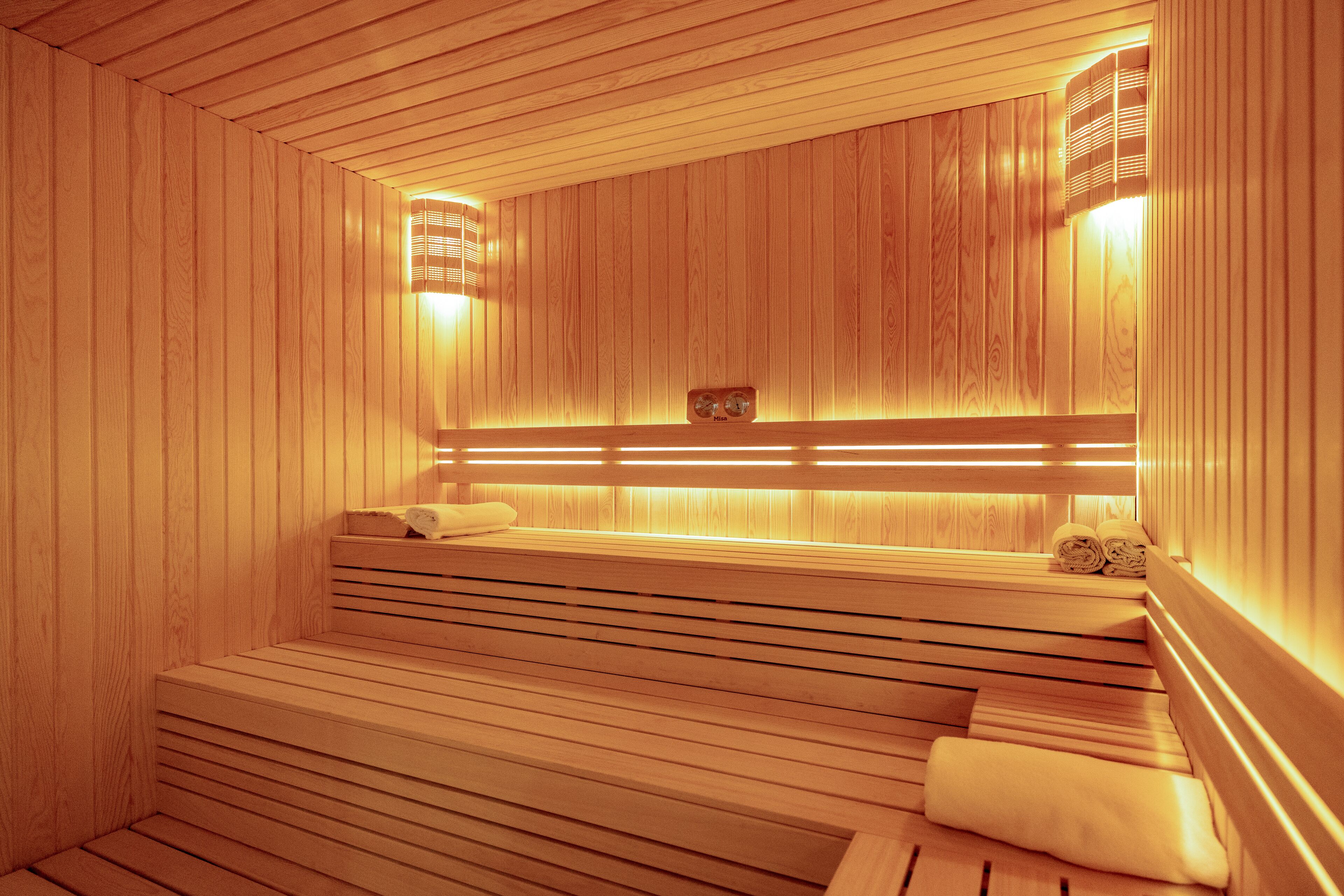 Un sauna en bois, doté de bancs et d’une banquette, d’un porte-serviettes et d’un radiateur fixé au mur.