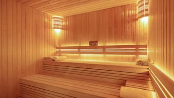 Un sauna en bois, doté de bancs et d’une banquette, d’un porte-serviettes et d’un radiateur fixé au mur.