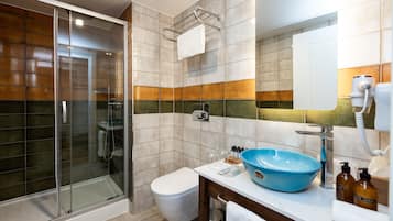 A modern bathroom with a glass shower enclosure, a white toilet, a blue sink, and a mirror above the sink.