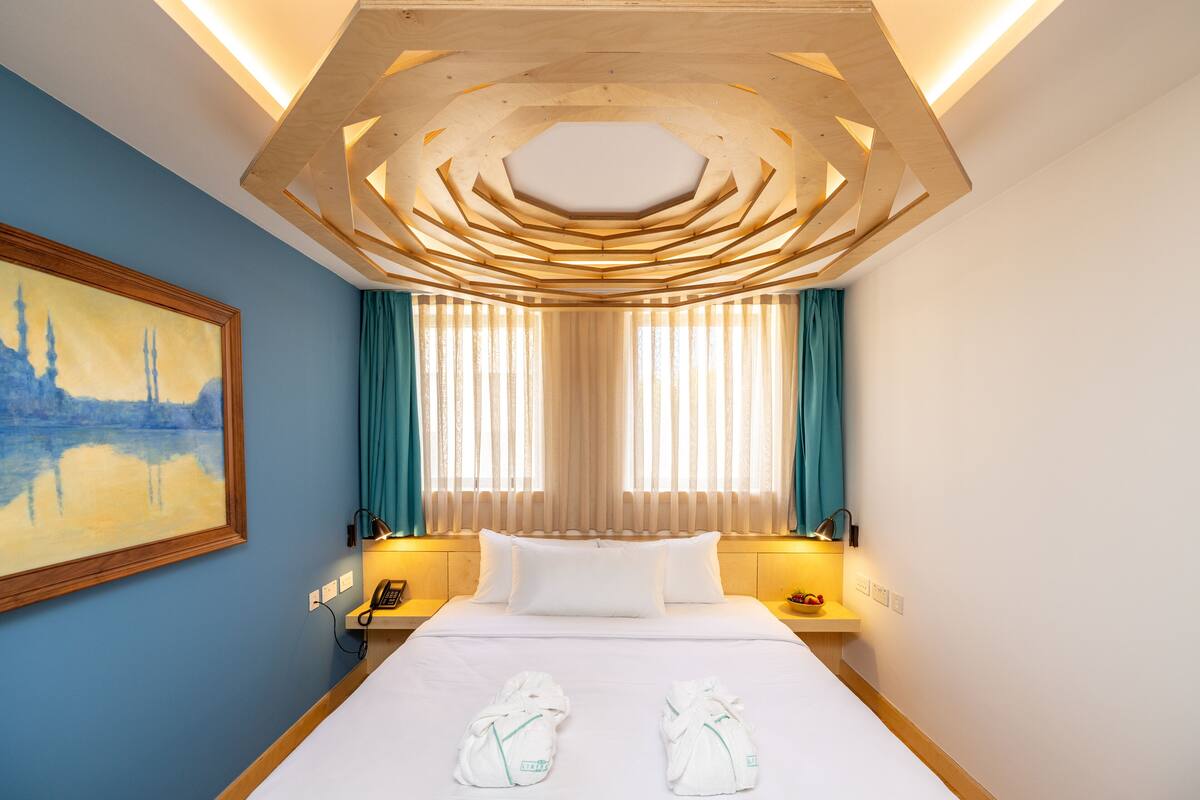 Une chambre d’hôtel avec un grand lit, deux tables de chevet, un tableau au mur et un décor de plafond original.