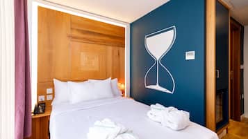 Een hotelkamer met een bed, houten hoofdeinde, een wandklok en een handdoekrek met handdoeken.