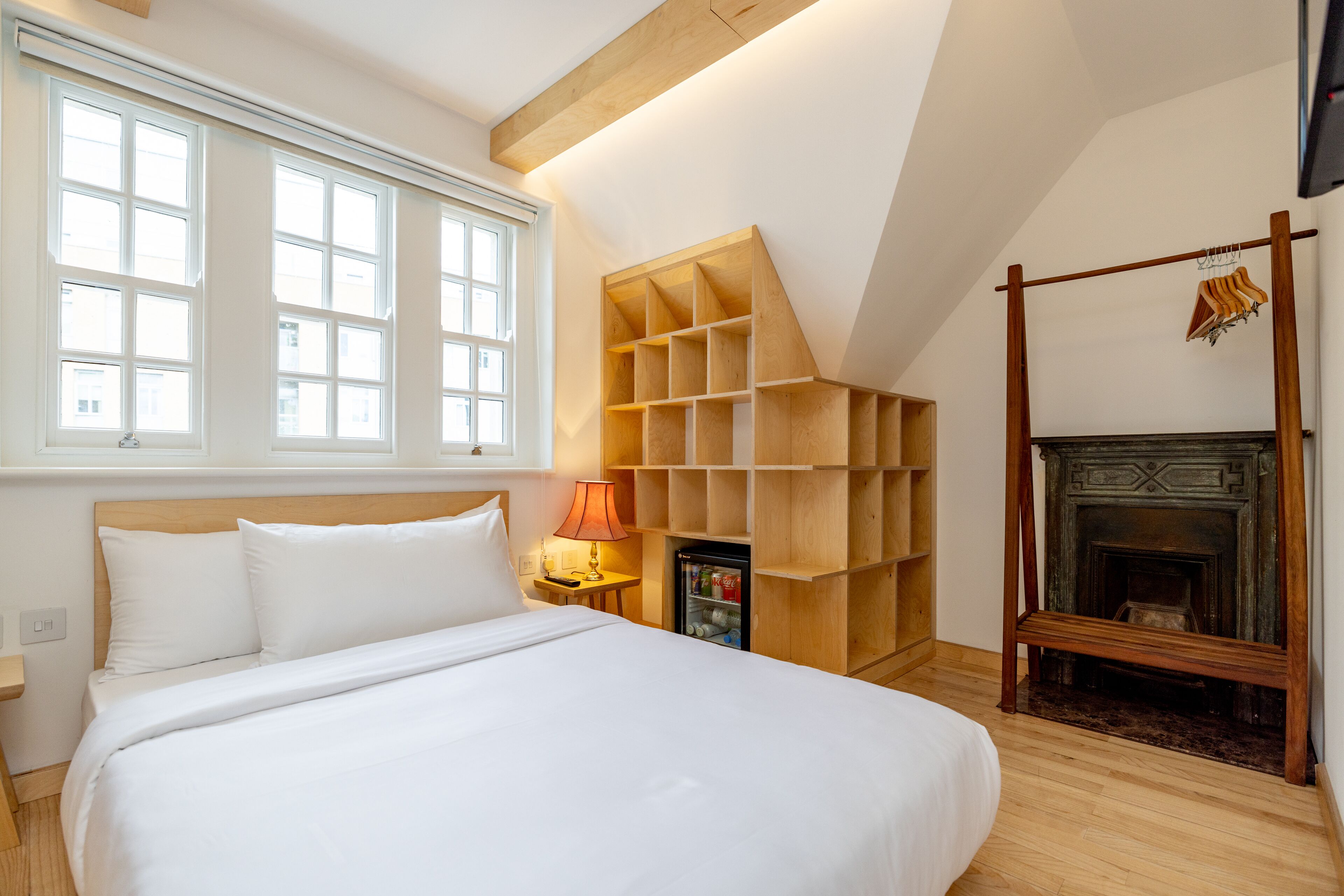 A bedroom with a large bed, a wooden shelving unit, a fireplace, and a window with multiple panes.