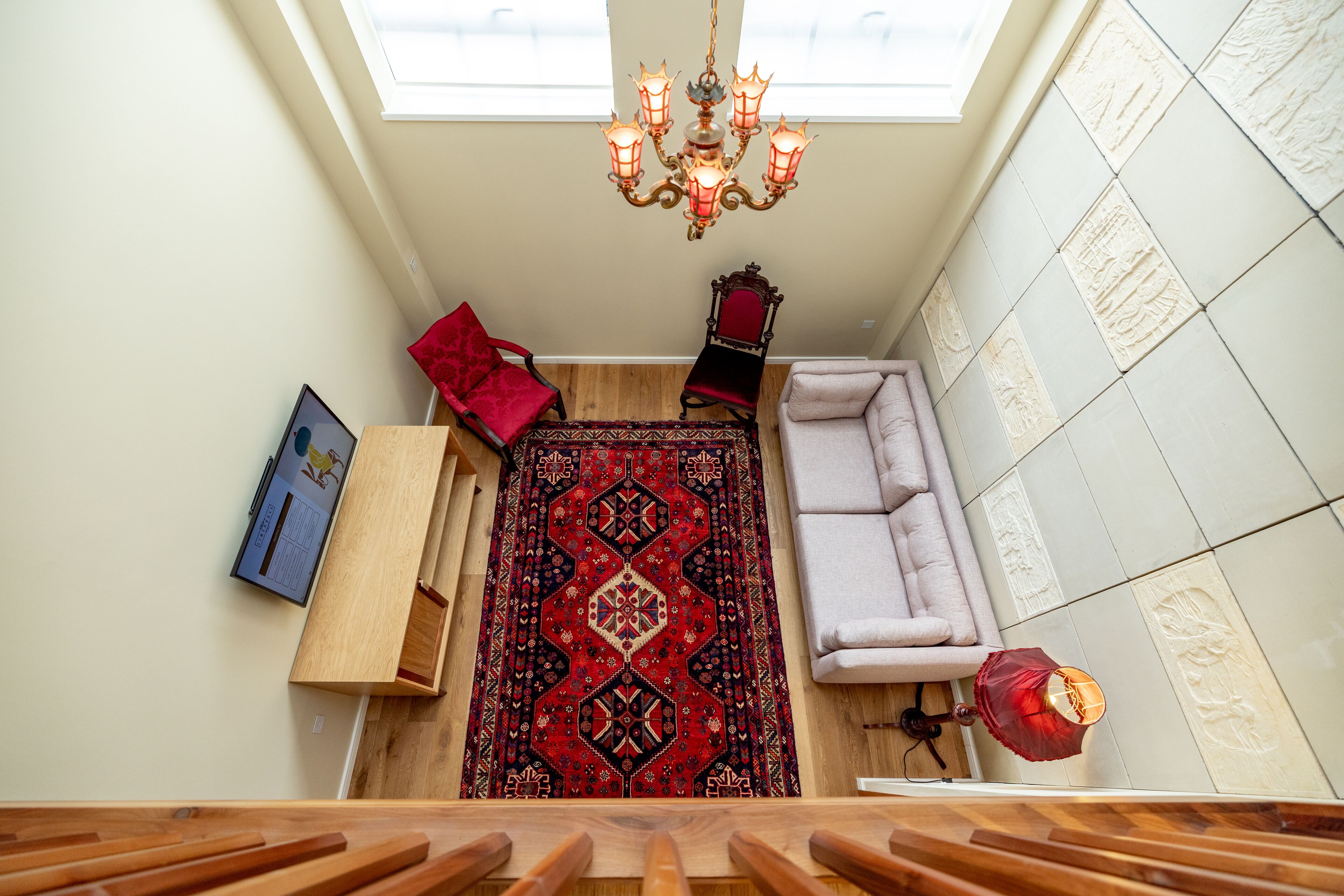 A room with a red patterned rug, a wooden bench, a red chair, a white sofa, and a chandelier.