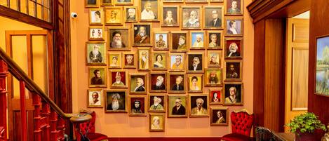 Un amplio vestíbulo con suelo de madera, alfombra roja y una pared decorada con numerosos retratos enmarcados.