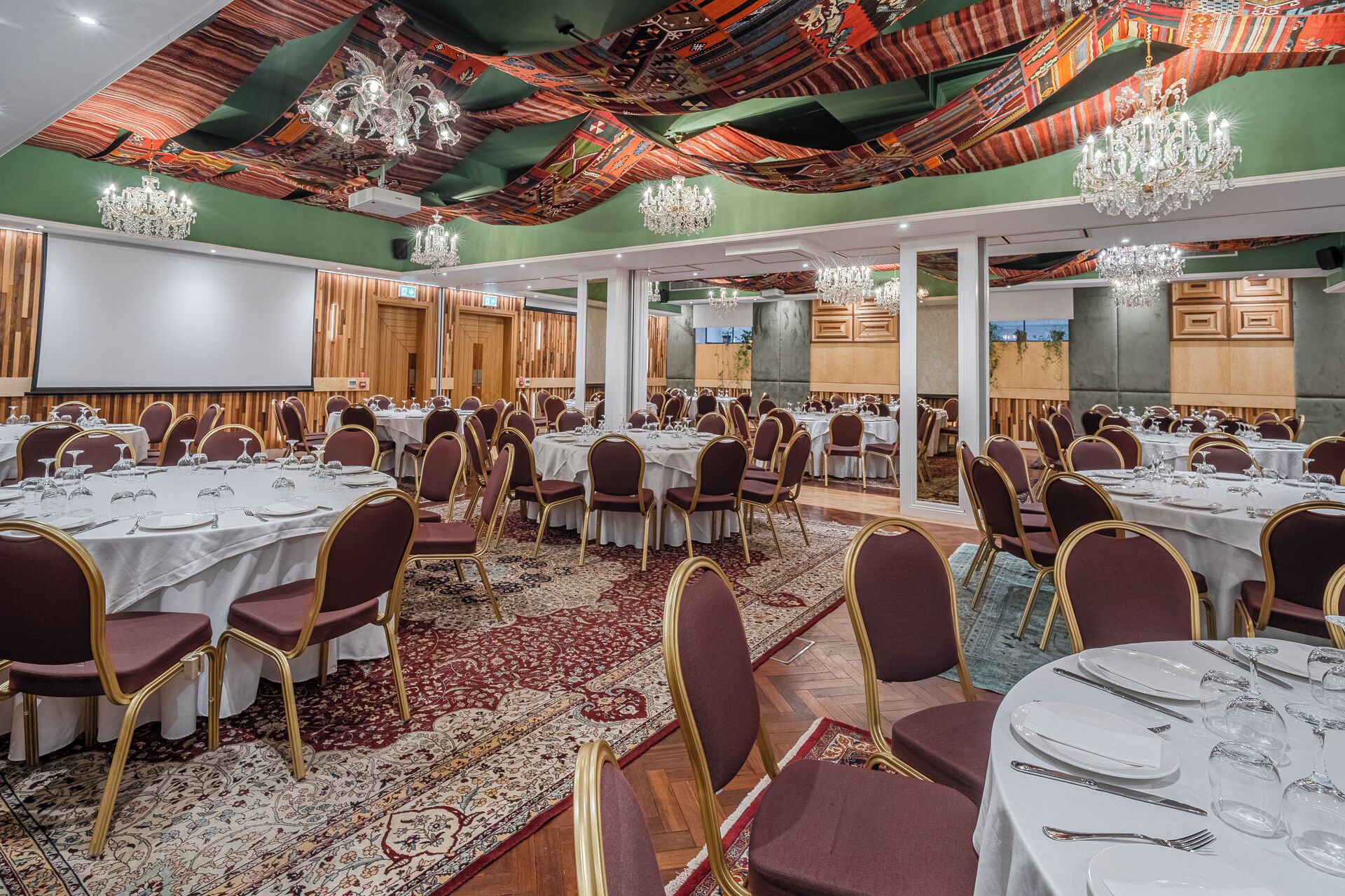 A banquet hall with round tables, red upholstered chairs, and chandeliers.