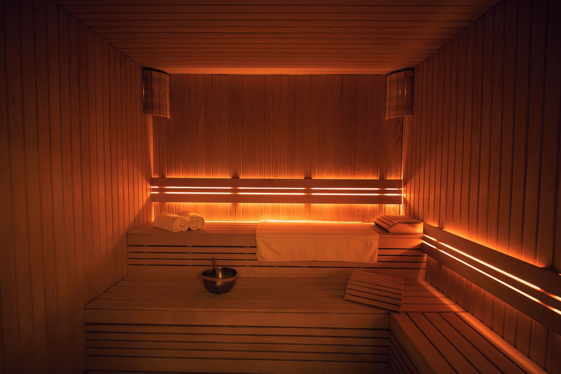 A sauna with wooden benches, a bench with towels, and a bowl.