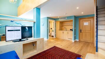 A modern hotel lobby with a reception desk, a television displaying hotel information, a kitchen area, and a wooden door.