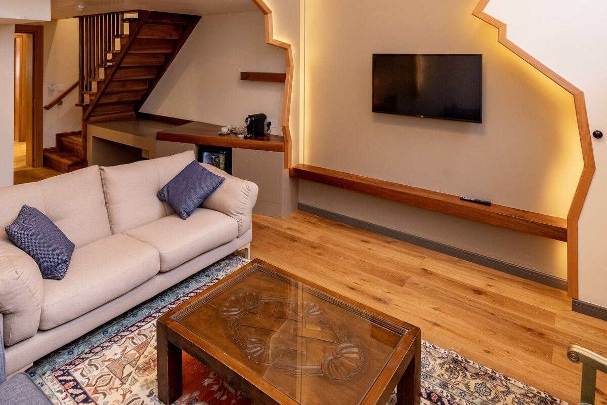 Un salon moderne avec un escalier en bois, un téléviseur à écran plat fixé au mur et un tapis à motifs.