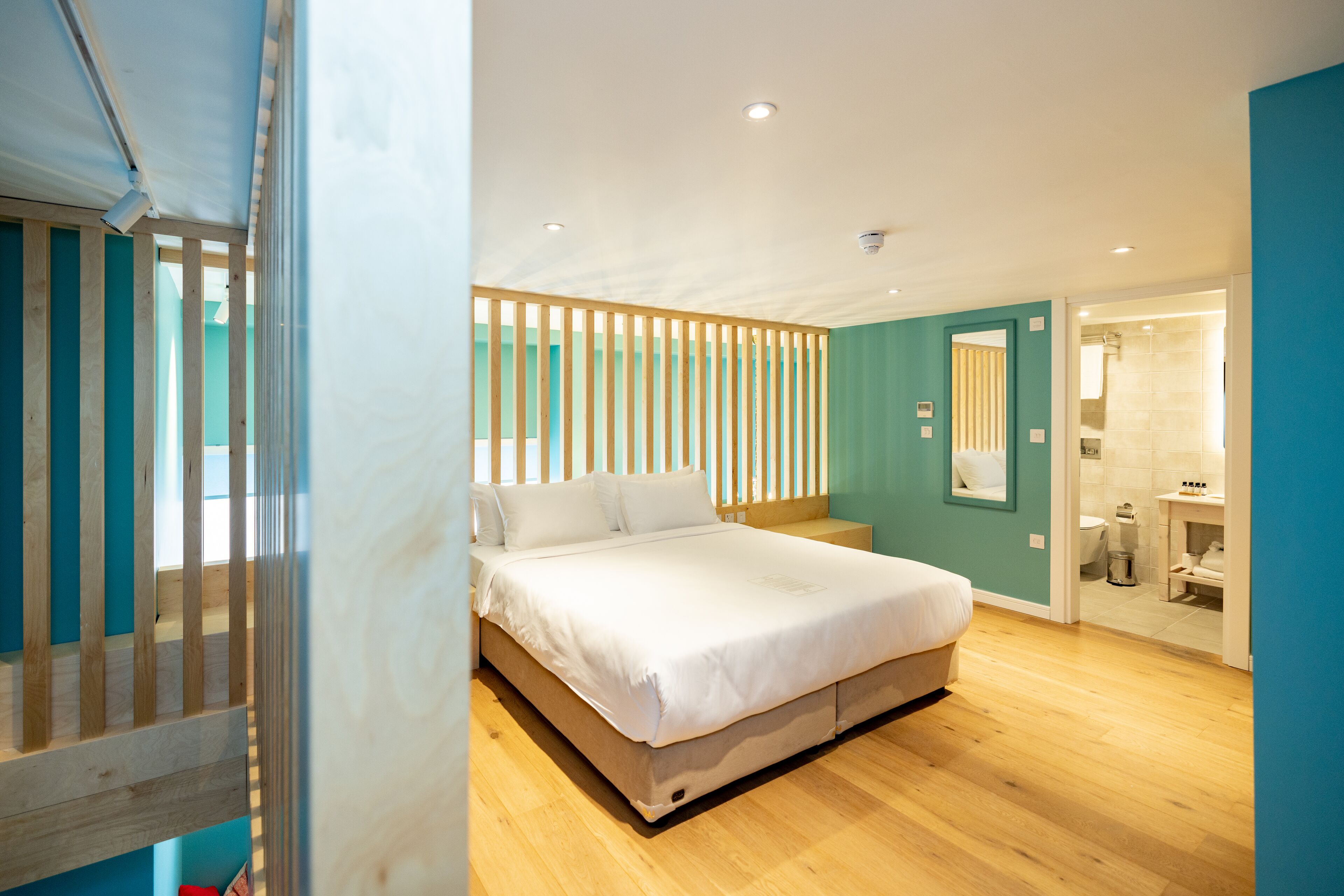A modern bedroom with a large bed, wooden slats, and a view into the bathroom.