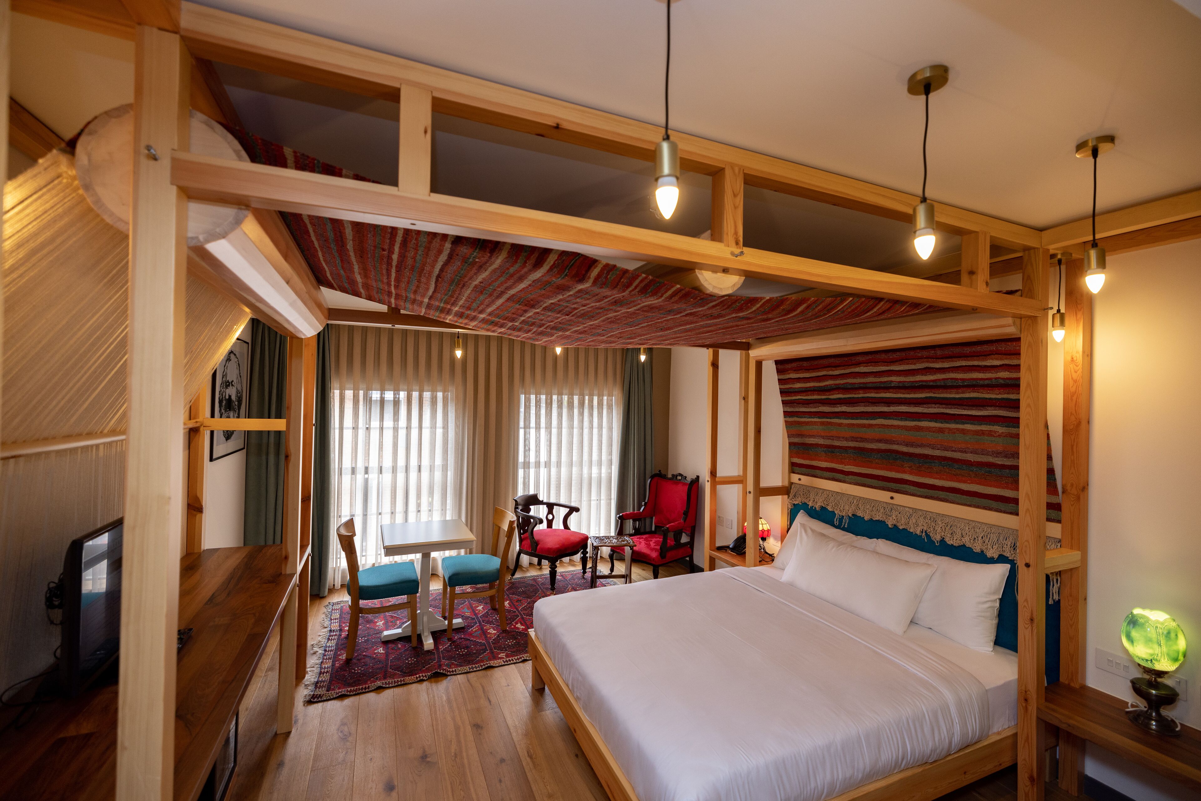 Een slaapkamer met een houten bedframe, een bureau, twee stoelen, een televisie en een raam met gordijnen.