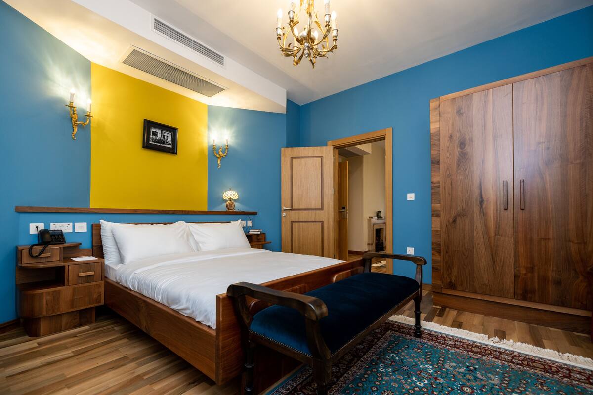 Une chambre avec un lit en bois, un banc, une armoire et un tapis à motifs.