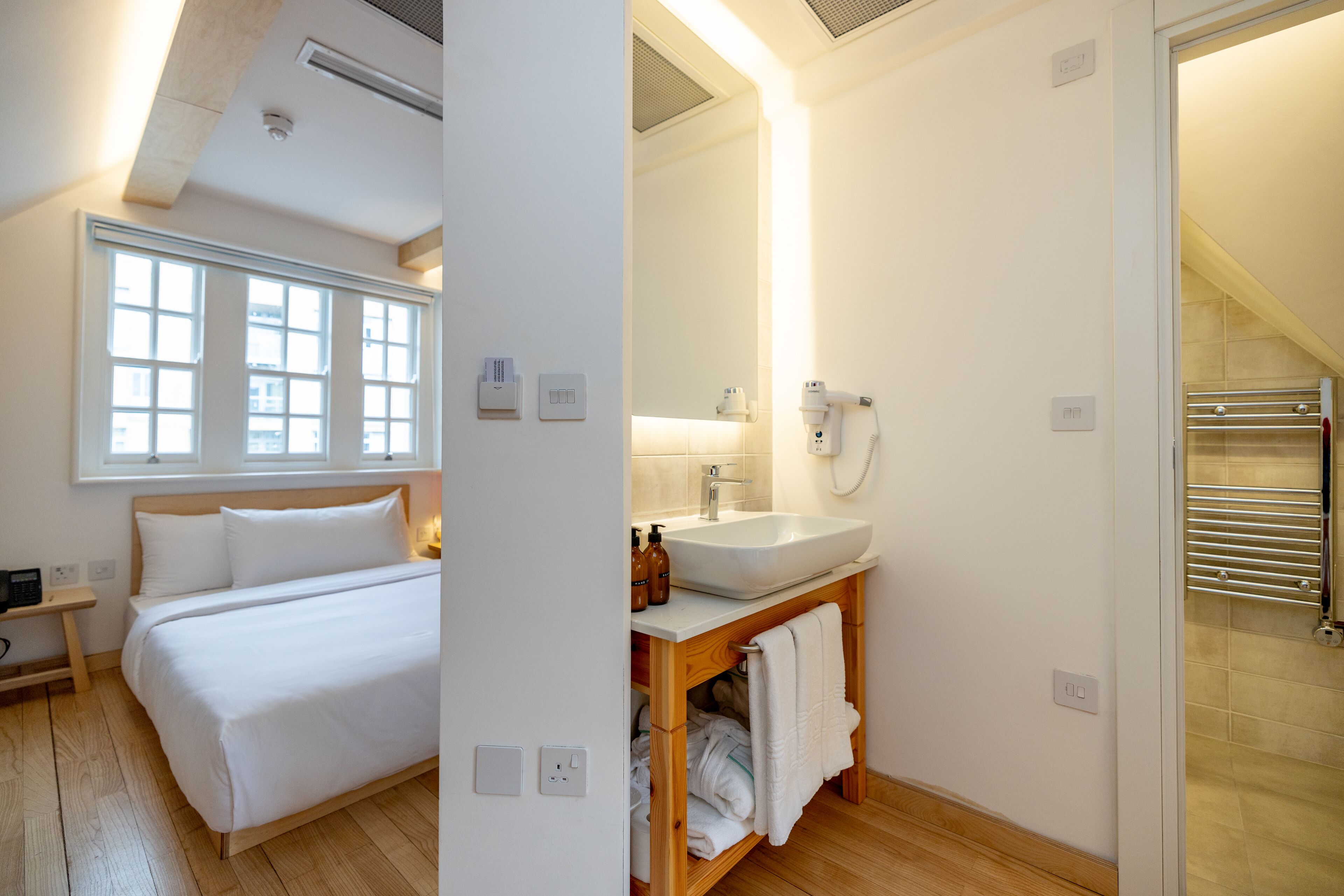 Quarto de hotel moderno com uma cama grande, uma toucador de madeira com pia e área de chuveiro.