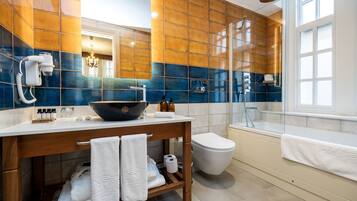 A modern bathroom with a large mirror, a wooden vanity, a black bowl sink, a toilet, and a shower area.