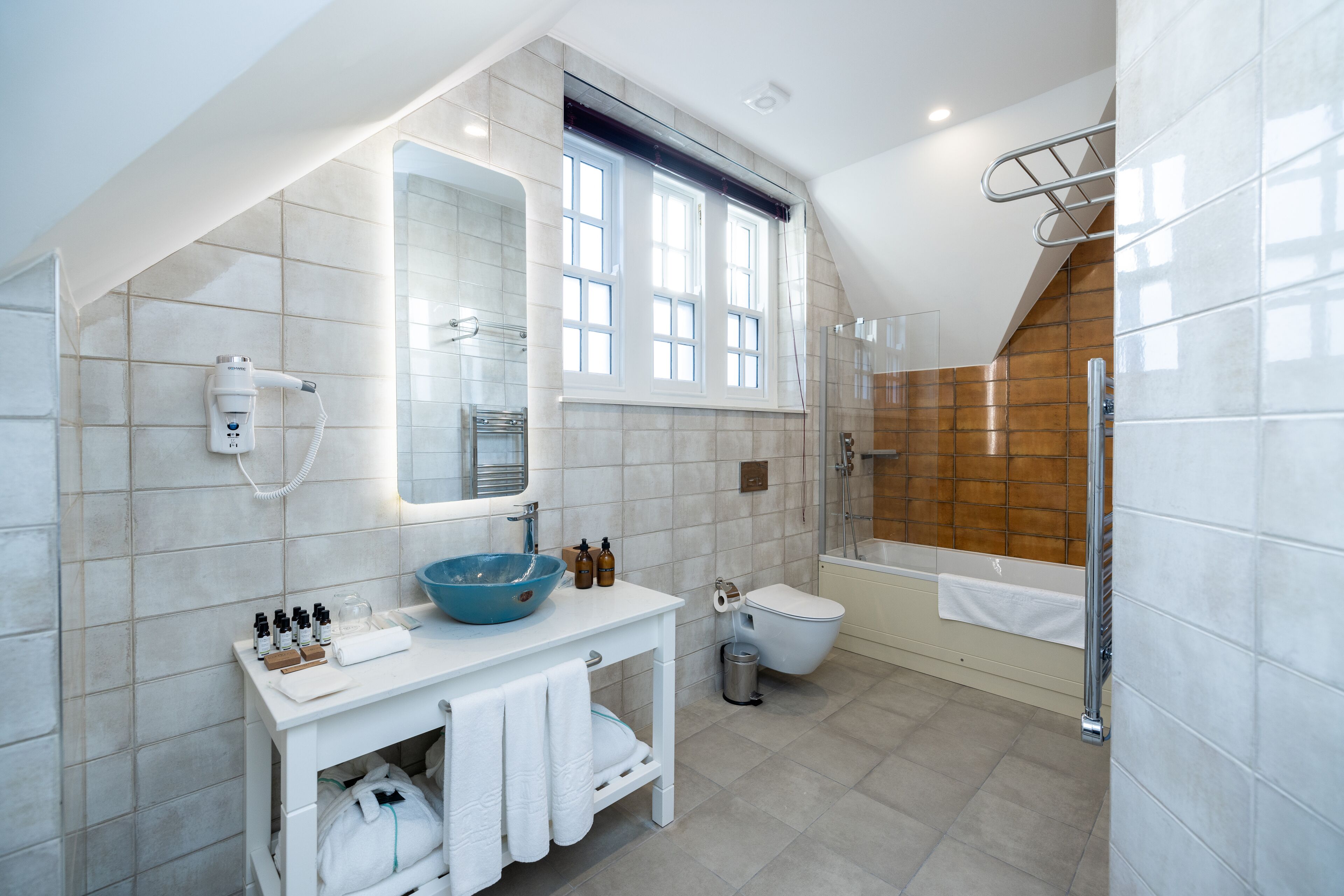 A modern bathroom with a white vanity, a blue basin, a toilet, and a bathtub.