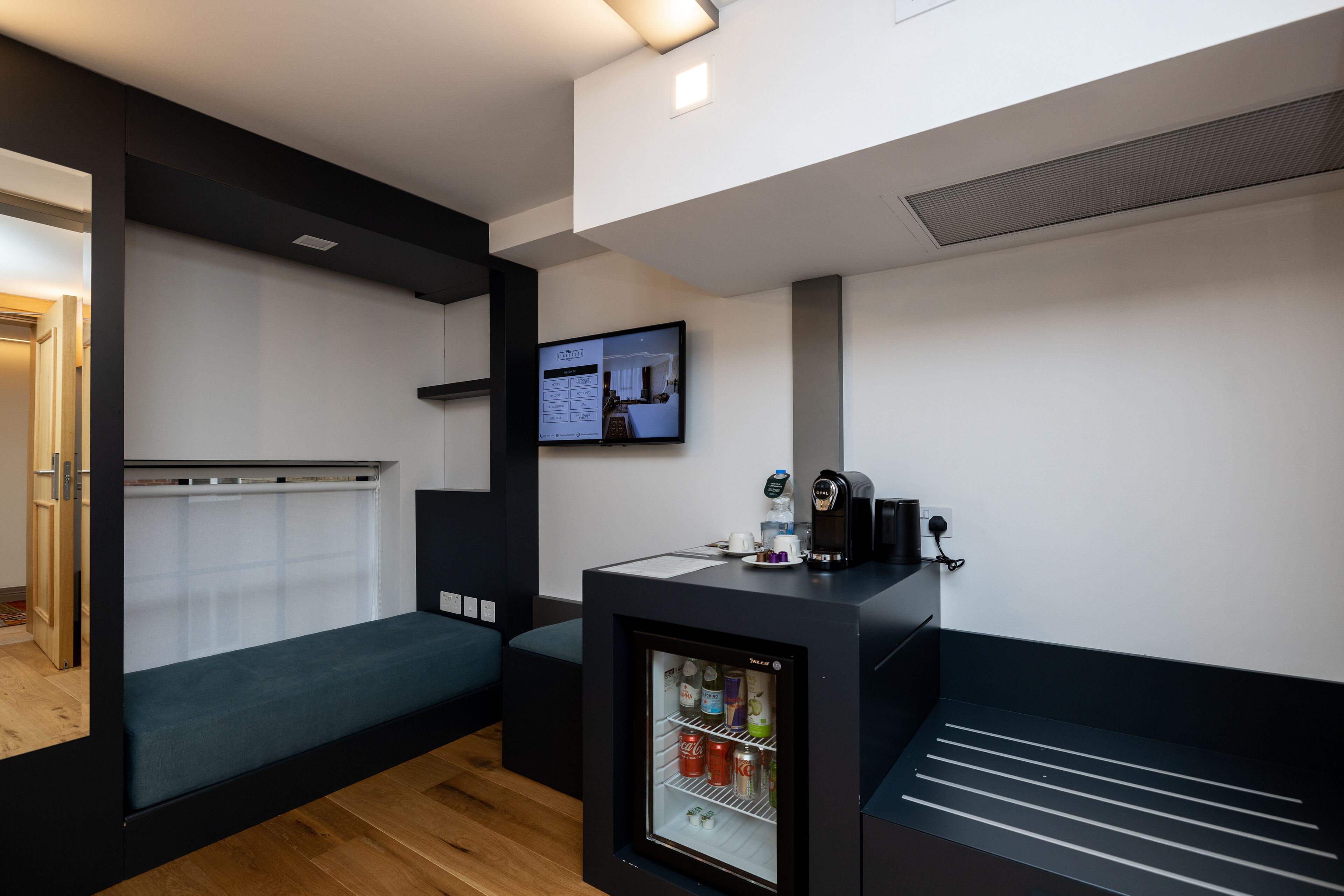 A compact hotel room with a bed, a small kitchenette, a refrigerator, and a television.