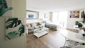 A modern living room with a glass coffee table, floral sofa, and a dining area with a white table. - 1610 🌸 free parking 🚙🅿️, fast WIFI💻 (Honolulu)