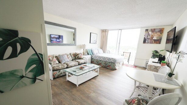 A modern living room with a sofa, a glass coffee table, and a dining area with a table and chairs. - 1610 🌸 free parking 🚙🅿️, fast WIFI💻 (Honolulu)