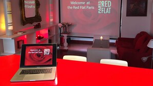 Un salon moderne avec un canapé rouge, un ordinateur portable et un écran affichant le message : « Bienvenue au Red Flat Paris ».