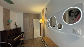 Une pièce avec un piano, un miroir orné de cercles lumineux et une porte.