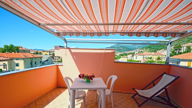 Ein Balkon mit Tisch und Stühlen, einem Hängesessel und Blick auf eine Stadt und Berge.
