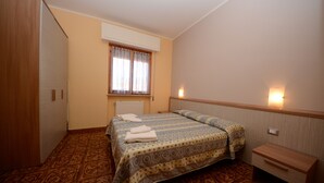 Ein Schlafzimmer mit Teppichmuster, einem Bett mit einem Muster auf der Bettdecke, einem Nachttisch, einem Kleiderschrank und einem Fenster mit Vorhängen.