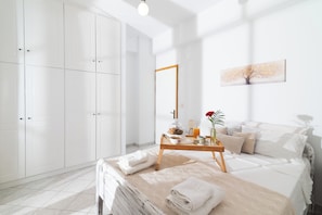 A hotel room with a bed, a bedside table with a vase and a lamp, a large wardrobe, and a painting on the wall.