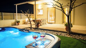 A hot tub with two glasses of red wine, surrounded by a patio area with potted plants and a building in the background. - Family friendly holiday home  (Neo Kalamaki)