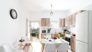 A modern kitchen with white cabinets, a refrigerator, and a dining area with white chairs and a glass table. - Family friendly holiday home  (Neo Kalamaki)