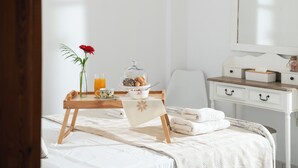 A neatly made bed with a white bedspread, a wooden bedside table with a glass bowl, a red flower, and a tray with breakfast items. - Family friendly holiday home  (Neo Kalamaki)