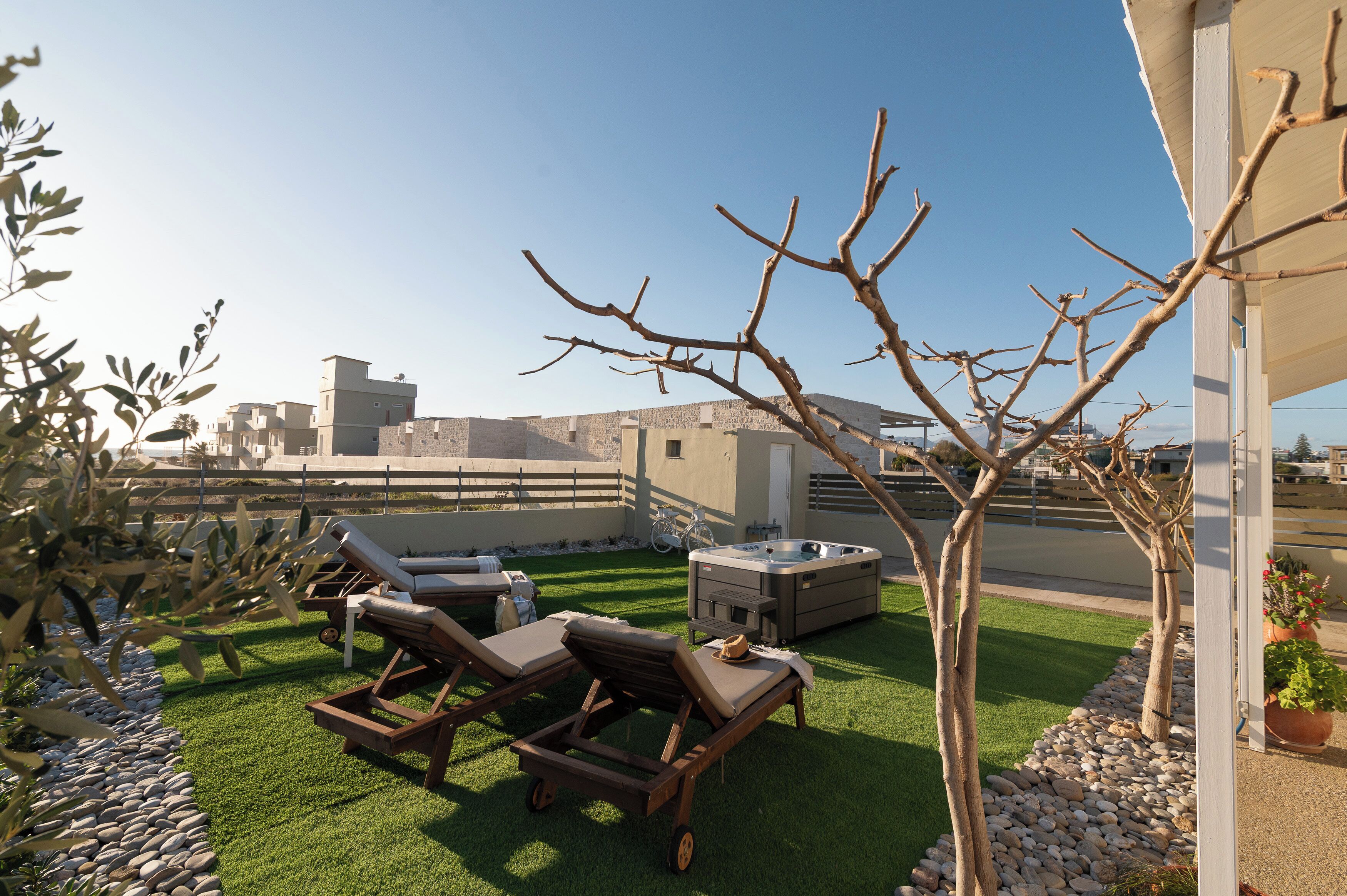 Una terraza en la azotea con dos sillones de descanso, una bañera de hidromasaje y un pequeño árbol.